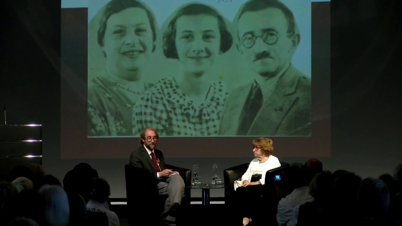An einem Tisch sitzen zwei Personen im Gespräch an einem niedrigen Couchtisch: rechts Hanni Levy, links Aubrey Pomerance