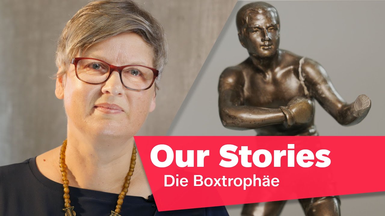 Portrait photo of Leonore Maier, in the background a damaged statue of a boxer, in the lower right corner of the picture the inscription “Our Stories: Die Boxtrophäe” (The Boxing Trophy).