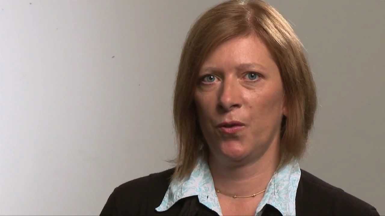 Woman with reddish blond hair looks at the camera and speaks.