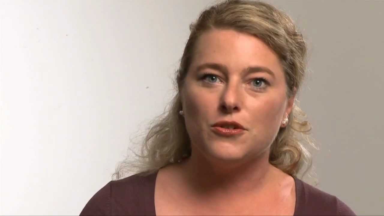 Woman with wavy hair speaks looking at camera.