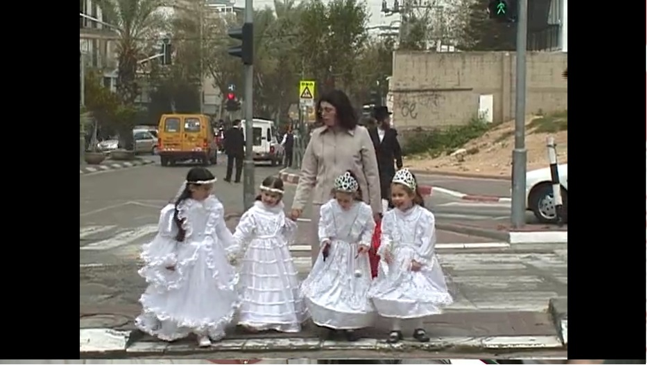 Eine Frau führt vier junge Mädchen in weißen Brautkleidern über eine Straße.