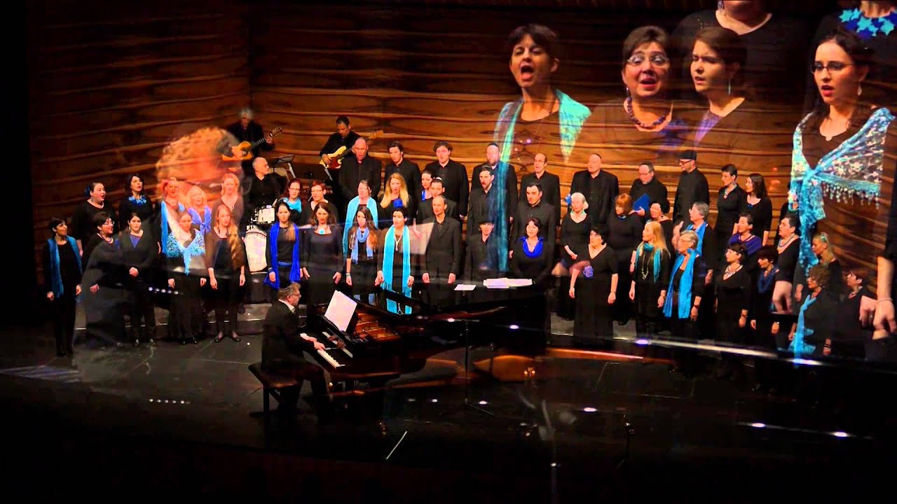A choir of about 40 people on a stage with grand piano accompaniment.