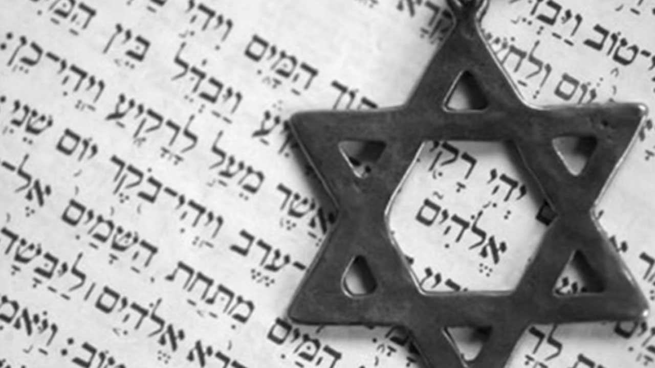 Foto von silbernem Davidsternanhänger vor hebräischer Schrift auf Papier.