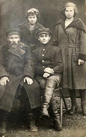 Black-and-white group photo: a man with a beard and a boy, seated, with a younger and older girl standing behind them, all wearing overcoats