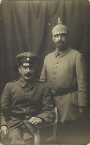 Schwarz-weiß-Foto: Zwei uniformierte Soldaten, der eine sitzend, der andere stehend und mit Pickelhaube, Atelieraufnahme.