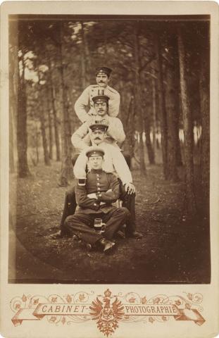 Schwarz-weiß-Foto: Vier uniformierte Soldaten mit Biergläsern, in einem Waldstück