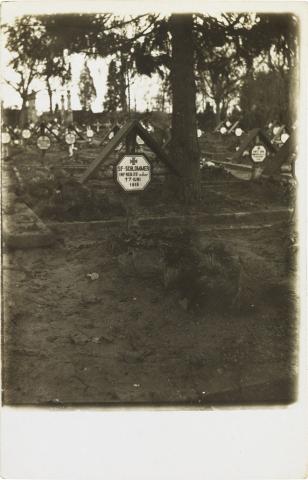 Schwarz-weiß-Foto: Grab mit Kreuz und Inschriftstafel, weitere Gräber im Hintergrund