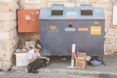 Ein Junge sitzt lesend vor einem Container am Straßenrand