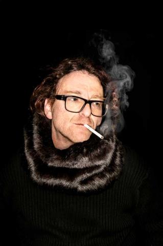 Man with mink scarf, glasses, and cigarette in front of a black background