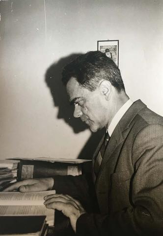 Black-and-white photograph of a man reading a book at a desk