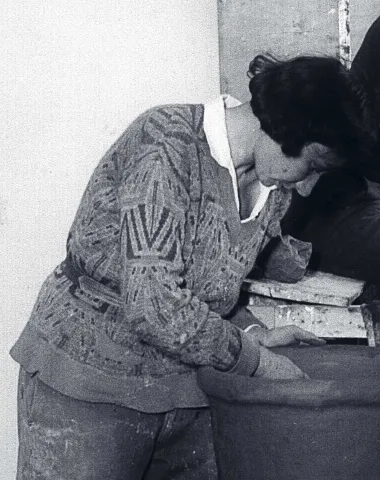  Black and white photograph of a woman working on a pottery vase at a potter's wheel.