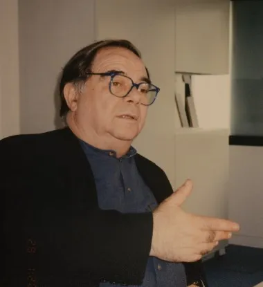 Portrait von Amnon Berzel: Ein Mann im Halbprofil mit dunklen schwarz-grauen Haaren und einer Brille mit schwarzem Rand. Er ist im Redefluss und gestikuliert mit seiner rechten Hand. 