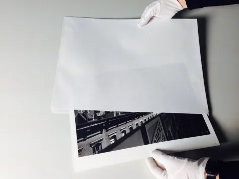 zwei Hände mit weißen Handschuhen halten das Foto The Elevated and Me von Ilse Bing im Umschlag