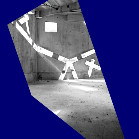 Schwarz-wei&szlig;-Foto eines noch im Bau befindlichen, leeren Raums, in dessen Betonw&auml;nden sehr schr&auml;ge Fenster sind, durch die Licht einf&auml;llt.