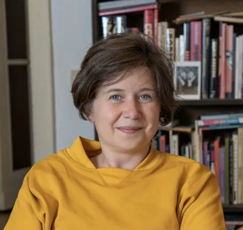 The picture shows a woman wearing a yellow sweater and smiling at the camera.