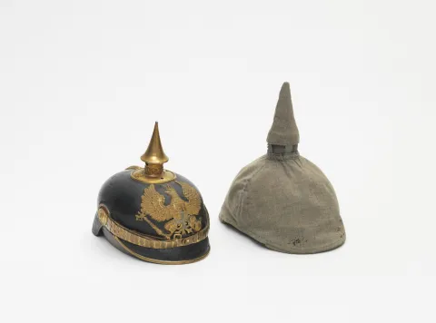 Eine Pickelhaube und ein Schutzbezug für die Pickelhaube auf grauem Grund