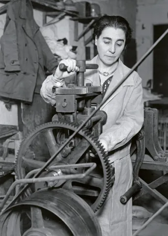  Black and white photograph of a woman at a machine.