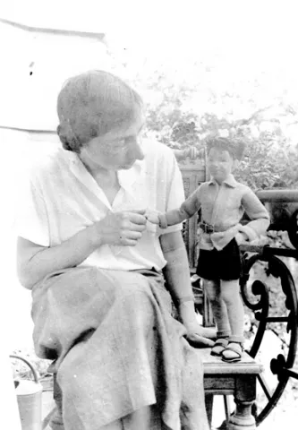 Schwarz-weiß-Foto einer Frau neben der rechts eine Puppe steht, deren Hand sie hält und die sie anblickt.