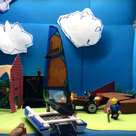 A crafted backdrop made of paper with a sailboat and Lego figures.