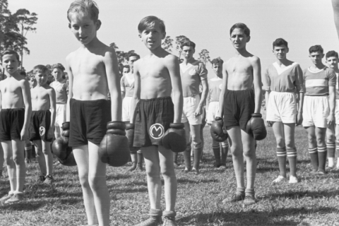 Children lined up on a lawn. They are wearing sports clothes and boxing gloves