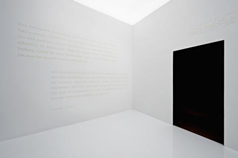 Raum mit weißer Schrift auf weißen Wänden, rechter Hand eine schwarze Tür