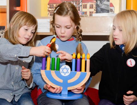Three children play with a colorful Hanukkah candelabra.