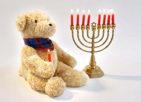 A teddybear holding a burning candle sits alongside an eight-branched lampstand