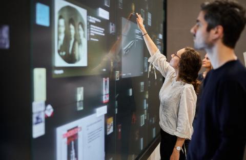 Three people stand in front of a wall of screens on which objects can be seen