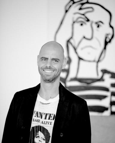 Black and white portrait of Eran Shakine in front of one of his drawings.