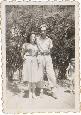  On the black and white picture Walter Frankenstein holds his wife Leonie in his arms. He wears a military uniform, Leonie a summer dress. They do not smile. Bushes grow in the background.