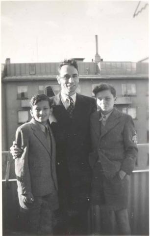 Rolf Rothschild stands in the middle of the black-and-white photo with his arms around the two boys. All three are wearing suits.
