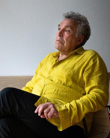 Photo of Frédéric Brenner in half profile, seated, wearing yellow shirt