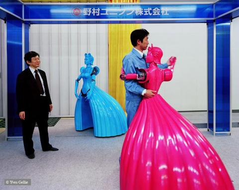 Foto: Ein Mann tanzt mit einem „weiblichen“ Roboter in magentafarbenem Ballkleid, während ein zweiter Mann zuschaut.