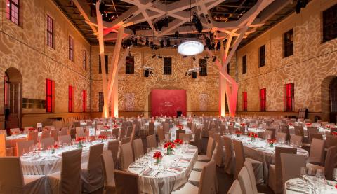 Glass Courtyard lit up with red and white lights, large dinning tables decorated with red flowers, silverware, and wine glasses fill the courtyard