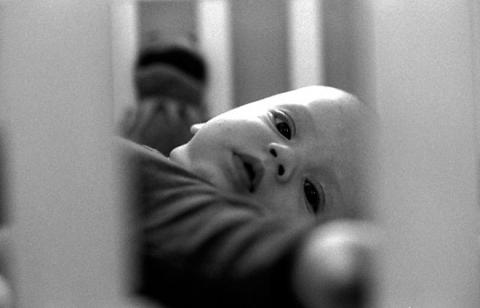 Schwarz-weiß Fotografie mit einem Kleinkind in einem Gitterbett