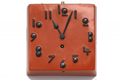 A red square clock with black numbers, the hand points to a few minutes past 11 o'clock
