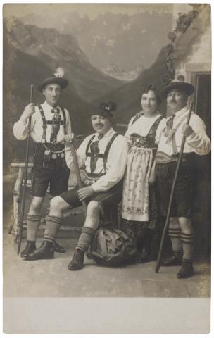  Black and white photo of four people in traditional Bavarian costumes in front of a mountain range.