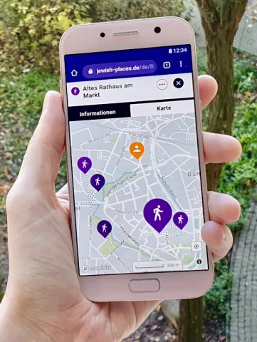 Eine Hand hält ein Smartphone, auf dem eine Karte mit bunten Ortsmarkern geöffnet ist.