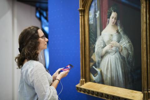 Junge Frau steht mit Smartphone und Kopfhörern vorm Porträt von Albertine Heine als Braut von August Theodor Kaselowsky