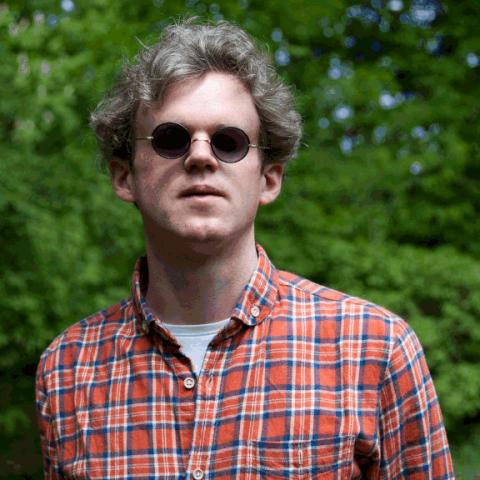 Portrait of Jonas Hauer with checkered shirt, sunglasses in front of a tree.
