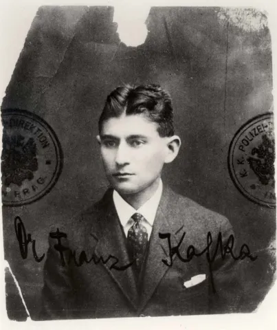Black and white passport photo of a young man with a gelled middle parting, stamp and signature on the photo: Dr. Franz Kafka.