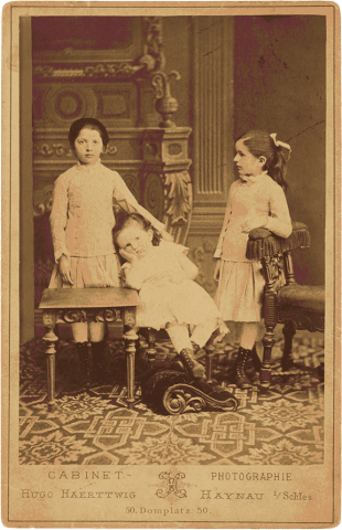 Historical black and white photograph of three children in white dresses.