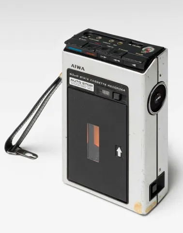 Fotografie eines Audioaufnahmegeräts für Tonkassetten mit schwarzer Lederschlaufe der Marke AIWA aus den 1970er Jahren. 