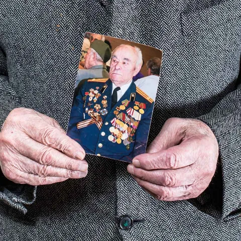 Hands holding a photo of a man wearing a uniform adorned with many ribbons and medals.