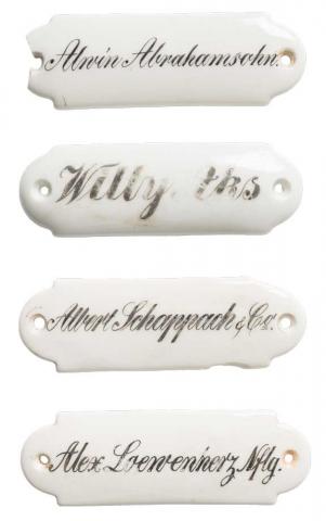 Four white porcelain signs one below the other with the names Abrahamsohn, Aks, Schappach and Loewenherz written in cursive.