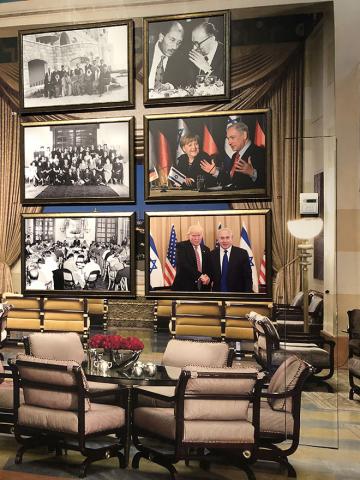 A wall with six large-format framed photos. In the foreground are armchairs and tables; the room looks like a hotel lounge