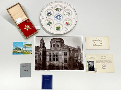 Ein goldener fünfzackiger Stern mit Hammer und Sichel, ein Seder-Teller, eine Postkarte aus Glowe, ein Foto der zerstörten Synagoge in der Oranienburgerstraße und verschiedene Ausweise