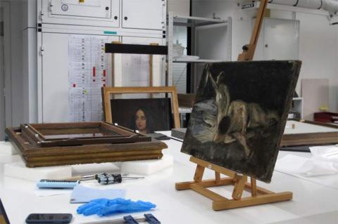 A painting on an easel on a table, with gloves and tools lying in front of the easel