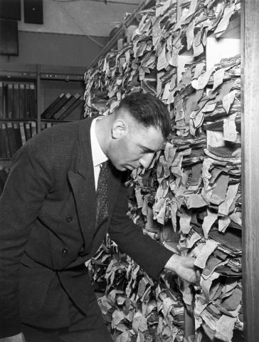 Black-and-white photo of a man in front of a shelving unit overflowing with file folders 