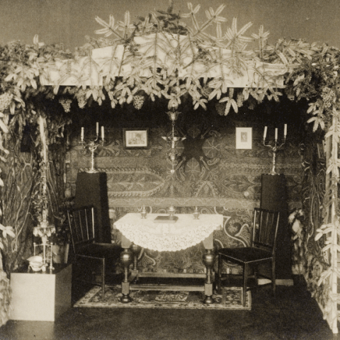 Black and white photo of a traditional Sukkah with table and chairs inside